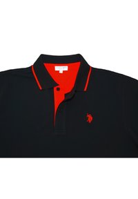 Černé polo tričko s kontrastním červeným límcem a knoflíkovou légou, které má malé červené logo na hrudi. Vyrobeno z bavlněného materiálu.