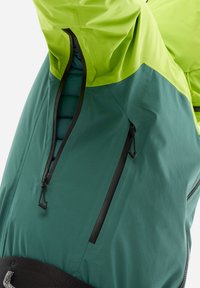 Veste imperméable avec un design bicolore, partie supérieure verte fluo et partie inférieure bleu sarcelle foncé. Comprend une grande fermeture éclair frontale et des cordons ajustables.