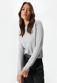 Vaaleanharmaa pitkähihaisen neuleen, jossa on pyöreä kaula-aukko ja ribattu hihansuu. Pehmeä rakenne, slim fit -muotoilu ja hienovarainen jousto mukavuutta varten.