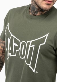 Olivovo zelené tričko vyrobené z bavlny, s veľkým bielym logom "TAPOUT" na hrudi, s okrúhlym výstrihom a krátkymi rukávmi.