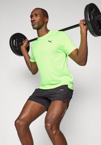 Neon green athletic t-shirt with short sleeves, paired with black shorts. The shirt features a black logo; the shorts have side slits.