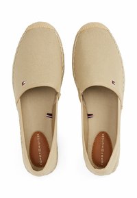 Espadrilles de lona beige con diseño sin cordones, suela de yute y sutiles acentos del logo de Tommy Hilfiger en los lados y en las plantillas.