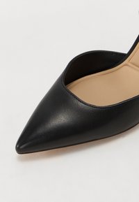 Chaussure femme noire à bout pointu avec tige en cuir lisse et semelle intérieure beige rembourrée, vue en gros plan en angle.