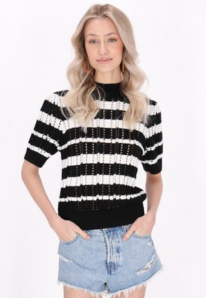 Suéter de punto a rayas en blanco y negro con mangas cortas, que presenta un cuello de canalé y detalles de tejido abierto. Combinado con pantalones cortos de mezclilla desgastados.