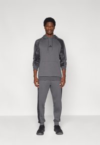 Γκρι φόρμα με κουκούλα που περιλαμβάνει φούτερ με μαύρα μοτίβα στα μανίκια και αντίστοιχο παντελόνι με μαύρες πλαϊνές λωρίδες. Κατασκευασμένη από απαλό ύφασμα.