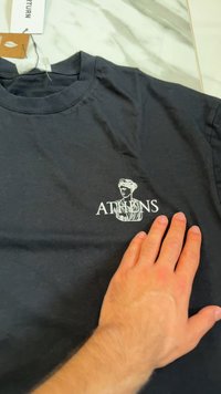 Must värvi puuvillane t-särk, millel on valge graafika büstist ja sõna "ATHEN" selle all. Ümmargune kaelus ja lühikesed varrukad.
