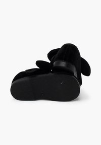 Zapatos de terciopelo negro con acentos de tela en las orejas y una suela de goma negra elegante. Presentan una superficie lisa y un cierre de correa seguro.
