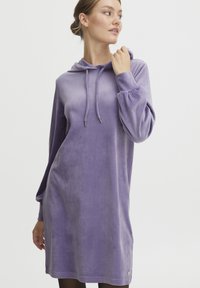 Lila hoodieklänning i mjukt, sammetsliknande material med en avslappnad passform, dragsko i huvan och långa ärmar. Har en rundad nederkant.