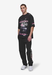 Black oversized t-shirt with graphic prints in white and pink, paired with black joggers featuring red accents. White sneakers complete the look.