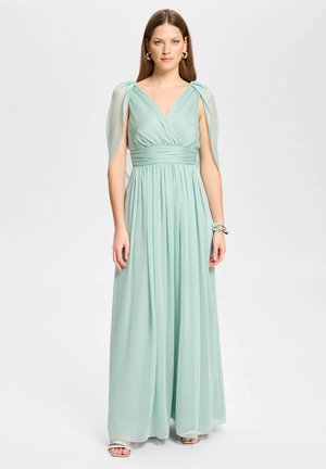 Femme portant une robe longue jusqu'au sol, vert menthe, sans manches, avec des épaules drapées et une taille froncée, debout devant un fond uni.