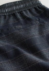 Navy stof met een subtiel plaidpatroon, voorzien van een golvende elastische tailleband. Zachte textuur met een licht glanzende afwerking en geweven details.