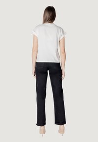 Maglietta bianca a maniche corte con risvolti, abbinata a pantaloni neri a vita alta. Entrambi i capi presentano un design minimalista e una texture liscia.