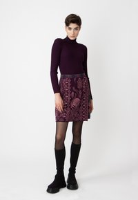Dunkellila gerippter Rollkragenpullover kombiniert mit einem gemusterten Rock mit floralen Designs und einem bunten Bund, getragen mit kniehohen schwarzen Stiefeln.