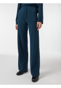 Pantalones de pierna ancha en un suave tejido de punto en un tono verde oscuro, con cintura elástica y detalles en hardware plateado. Combinados con calzado negro.