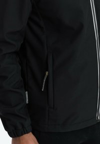 Giacca nera con texture liscia, dotata di una tasca con zip e polsini elasticizzati. Include una zip frontale argentata e dettagli di cucitura discreti.