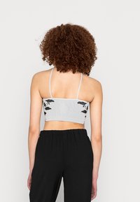 Top cropped cinza com textura em canalé e alças finas, adornado com bordados florais pretos nas costas. Combinado com calças pretas soltas em um corte relaxado.