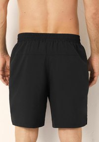 Zwarte sportieve shorts met een elastische tailleband, een gladde textuur en zijopeningen aan de zoom. Ontworpen voor comfort en bewegingsvrijheid.