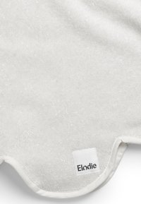 Valkoinen tekstiilimatto, jossa on pehmeä, teksturoitu pinta, pyöristetyt reunat ja ommeltu etiketti, jossa lukee "Elodie" mustalla värillä yhdessä kulmassa.