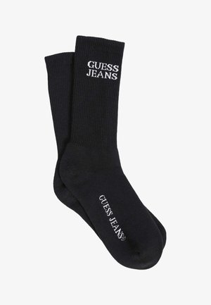 Schwarze gerippte Socken mit weißem "GUESS JEANS" Logo-Text an Bund und Fußbereich. Hergestellt aus einem glatten, dehnbaren Stoff.