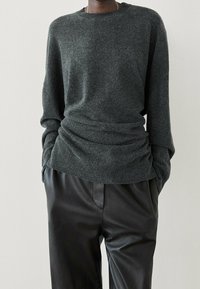 Pull gris foncé en maille avec un col rond et des détails froncés à la taille, associé à un pantalon en cuir noir. Texture douce et coupe ample.