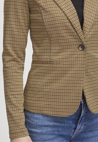 Blazer à carreaux jaune et marron, doté d'une fermeture à un bouton et d'une coupe ajustée. Le tissu présente une texture lisse avec des lignes subtiles.