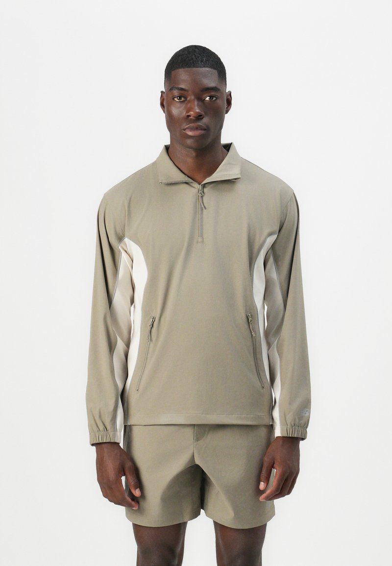 Haut à manches longues léger et zippé en olive avec des panneaux latéraux blancs ; associé à un short assorti olive ; texture lisse, coupe athlétique.