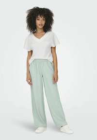 Haut blanc en V à manches courtes, associé à un pantalon large vert clair et des baskets blanches. Tissu souple et design décontracté.