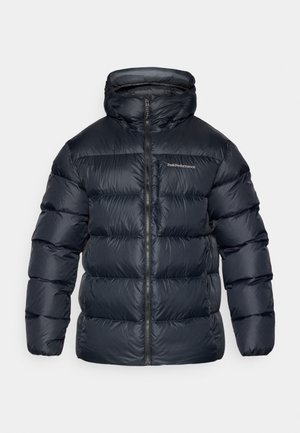 Temna puffer jakna z visokim ovratnikom, polnim zadrgo in šivnimi paneli. Na prsih je logo Peak Performance; gladka, sijoča tekstura.