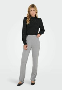 Juoda ilgomis rankovėmis tekstūruota palaidinė su nėrinių detalėmis, derinama su šviesiai pilkomis aptemptomis kelnėmis, turinčiomis du priekinius mygtukus ir tiesios linijos modelį.