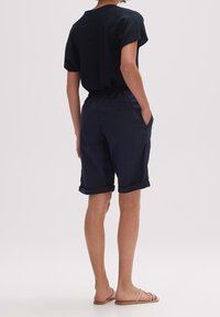 Czarna, teksturowana koszula z krótkim rękawem w połączeniu z granatowymi szortami z podwiniętymi mankietami i bocznymi kieszeniami, uzupełniona beżowymi sandałami.