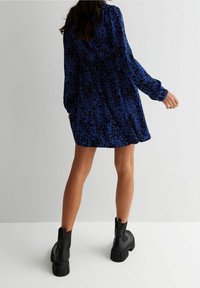 Abito con stampa animale blu, maniche lunghe, vita cinchata e gonna svasata. Abbinato a stivali alla caviglia neri con tacco spesso.