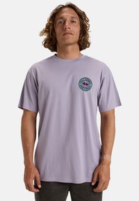 Camiseta de algodón de manga corta de color púrpura claro, con un gráfico circular en verde y rosa en la zona del pecho izquierdo.