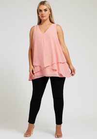 Persikofärgad, lager-på-lager ärmlös blus med V-ringning, tillverkad av lätt tyg, i kombination med svarta, figursydda byxor och silverfärgade klacksandaler.