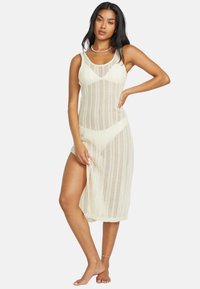 Strick-Cover-up-Kleid in Cremeweiß, mit ärmellosem Design, strukturiertem offenen Gewebe und einem seitlichen Schlitz bis zur Oberschenkelhöhe für zusätzliche Belüftung.