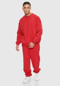 Rotes Sweatshirt- und Jogginghosen-Set, das sich durch eine entspannte Passform, Rippbündchen und einen kleinen Logoakzent auszeichnet. Der Stoff wirkt weich und glatt.