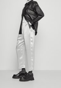 Svart läderskjorta med avslappnad passform, vita satinbyxor med tapered fit, och kraftiga svarta skor med snörning och texturerade sulor.