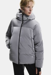 Szara kurtka puchowa z kapturem, z kontrastowym zamkiem, pikowaną fakturą i dwiema bocznymi kieszeniami. Minimalistyczne logo na brzegu.