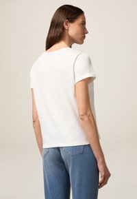 Weißes T-Shirt mit kurzen Ärmeln und runder Ausschnitt, aus weichem Baumwollmaterial, kombiniert mit hellblauen Jeans mit Gesäßtaschen und geradem Schnitt.