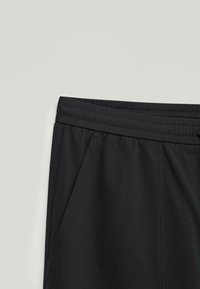 Pantalon de sport noir avec une ceinture élastique, deux poches latérales, et une texture de tissu lisse. Design simple et sans ornement.