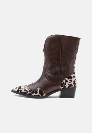 Bota de vaquero de cuero marrón de altura media con acentos moteados en negro y blanco en la puntera y el talón, costuras decorativas y un tacón bajo de bloque.