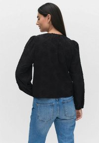 Svart texturerad blus med långa puffärmar, prydd med blommönster och en rynkad krage. Matchad med ljusblå denimjeans.