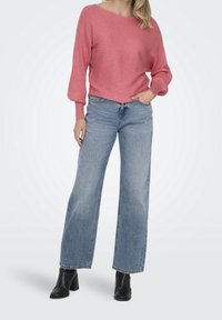 Rosa geripptes Strickoberteil mit weitem Ausschnitt, kombiniert mit hellblauen weit geschnittenen Jeans. Schwarze Knöchelstiefel runden das Outfit ab.