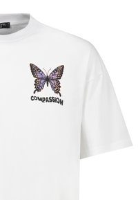 Weißes Baumwoll-T-Shirt mit einem lila und schwarzen Schmetterling-Graphic, unter dem das Wort "MITGEFÜHL" gedruckt ist. Kurze Ärmel und Rundhalsausschnitt.