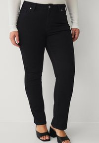 Schwarze Denim-Skinny-Jeans verfügen über ein klassisches Fünf-Taschen-Design, einen Knopfverschluss und eine glatte Textur. Kombiniert mit offenen Blockabsätzen.