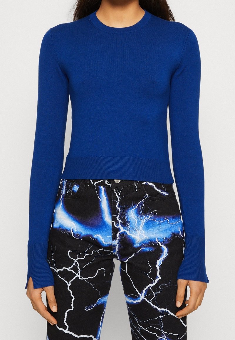 Personne portant un haut bleu ajusté à manches longues et un pantalon noir avec des motifs d'éclairs bleu vif et blanc.