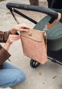 Béžová květinová taška se zipem, připevněná k rukojeti kočárku. Má malé růžové a zelené kvítky, hladký materiál a kovové kování.