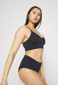 Sorte bralette med tynne stropper og bredt bånd, kombinert med høyt liv-sorte truser med en kontrasterende midje. Glatt stofffinish.