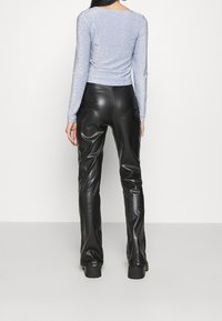 Lichtblauw langemouwen top met een glinsterende textuur, gecombineerd met hoge zwarte leren broek. Beide kledingstukken hebben een slim fit.