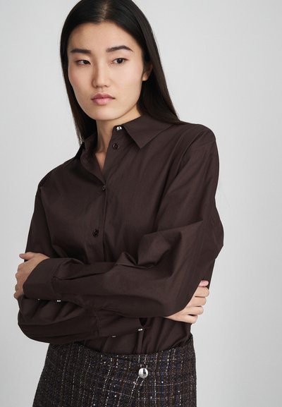 Chemise marron à boutons avec un col classique et des manches longues, fabriquée en tissu lisse. Associée à une jupe texturée multicolore.