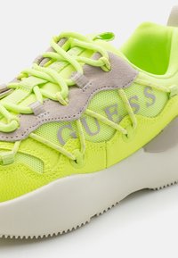 Neon yellow sneaker with mesh and textured leather, accented by grey suede. Features thick laces and a chunky white sole for traction.